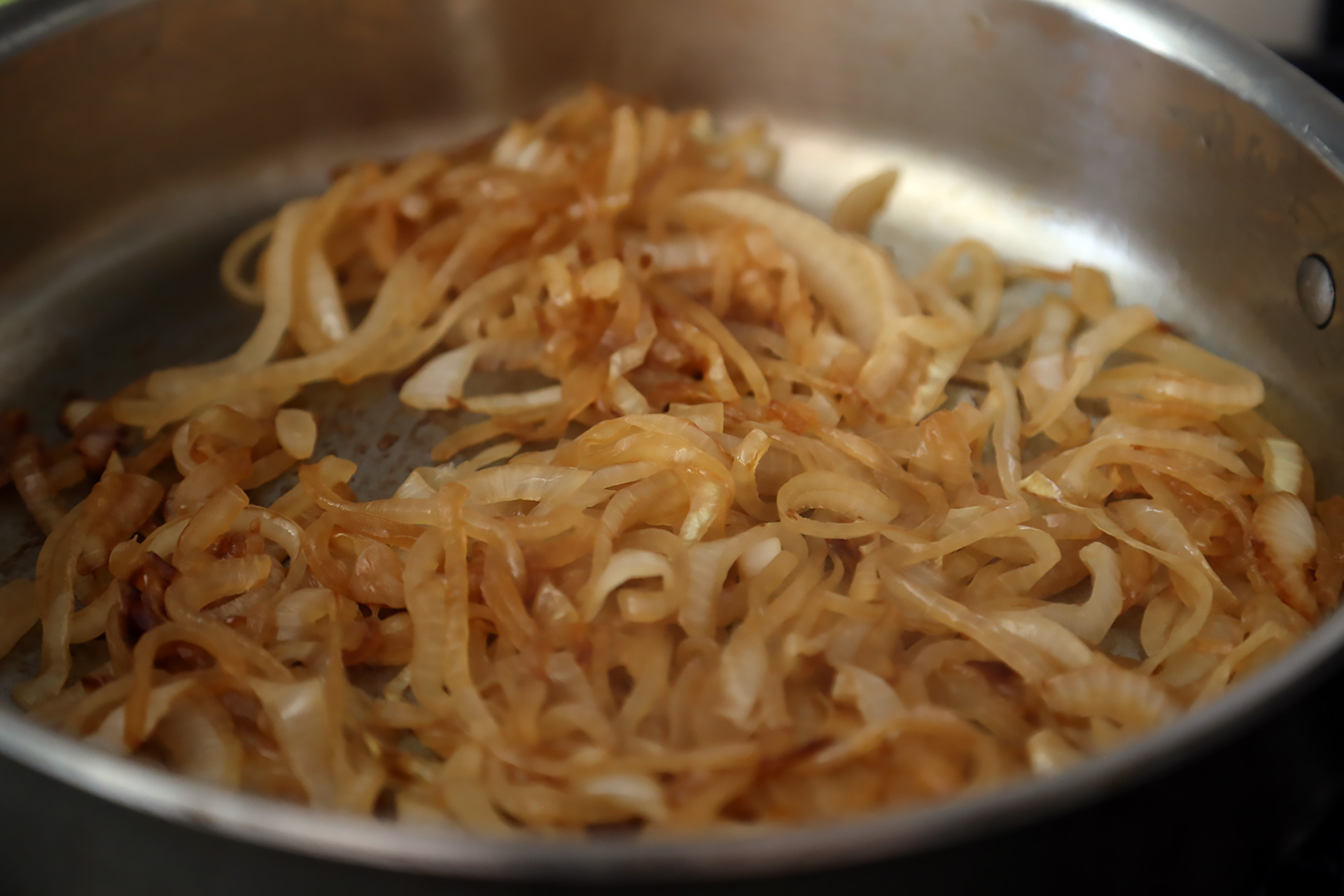 In a large saute pan over medium heat, warm the oil. Add the onions and a pinch of salt and cook, stirring, until they start to caramelize, about 15 minutes. Transfer to a bowl.