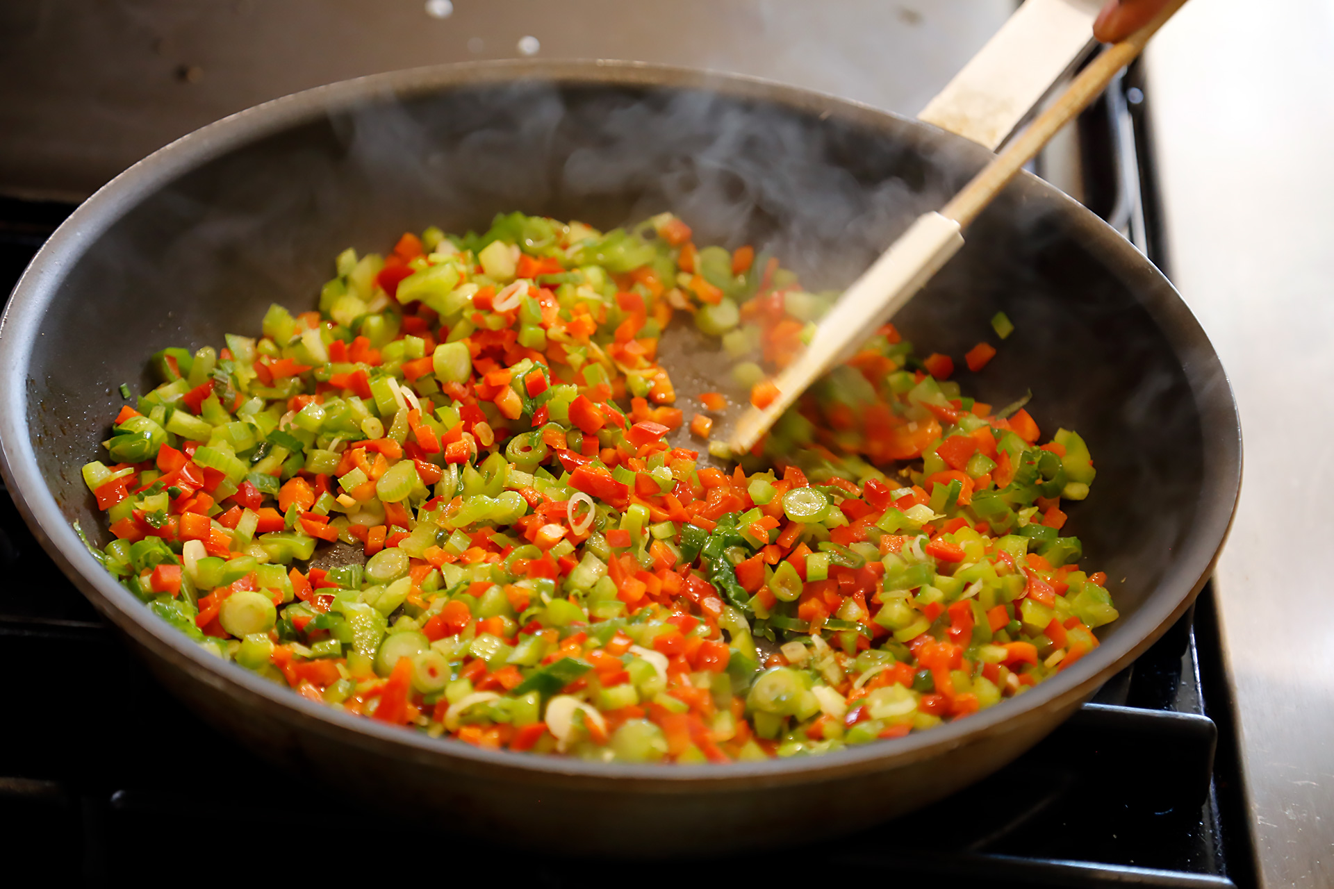 Heat oil in a large sauté pan until shimmering. Add bell peppers, scallions/green onions, and garlic.