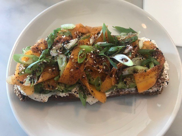 Sqirl, a popular eatery in LA's Silver Lake neighborhood, is known for its avocado toast. It features an entire avocado on a thick slice of country bread from a local bread-maker, with garlic creme fraiche and topped with hot pickled carrots and homemade za'atar.
