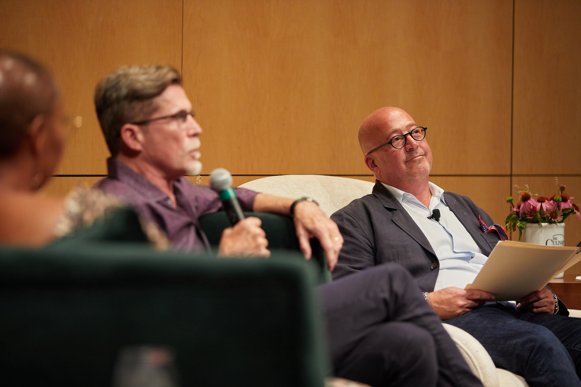 Andrew Zimmern listens on as Rick Bayless answers a question from the crowd.