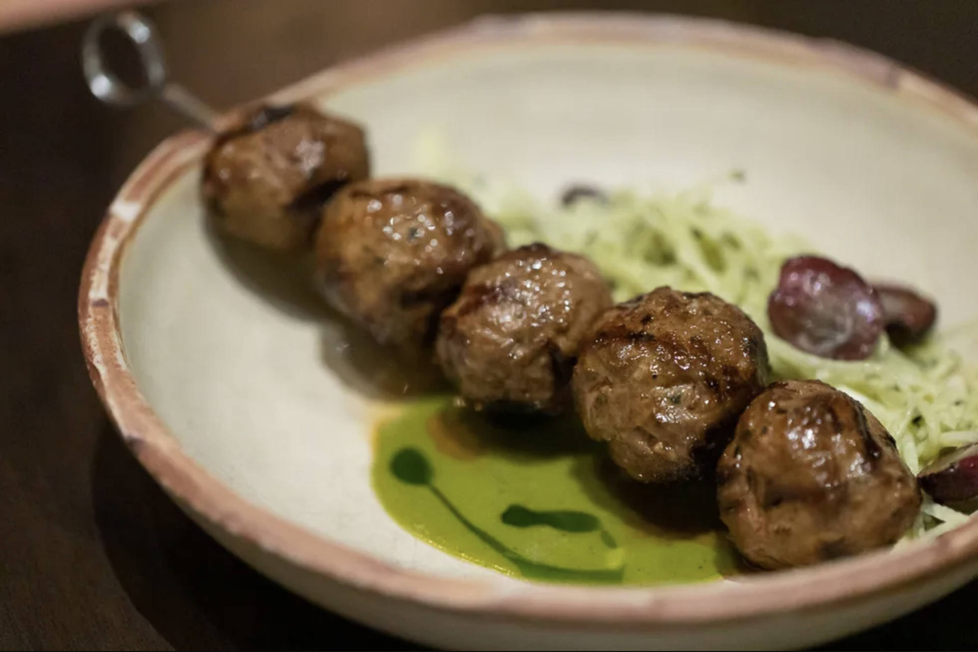 A skewer of five tender kefta meatballs, on a pool of cilantro vinaigrette, is served with a chilled salad of shaved jicama and halved grapes for a refreshing contrast.