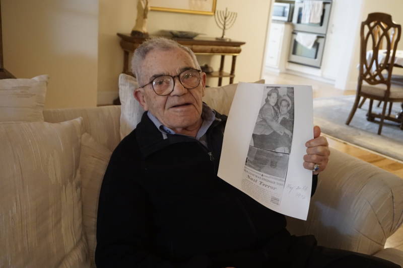 Ben Stern holds up a copy of a newspaper clipping show him and his wife after they came to the United States as Jewish refugees after World War II. Stern survived two ghettos, nine concentration camps and two death marches.