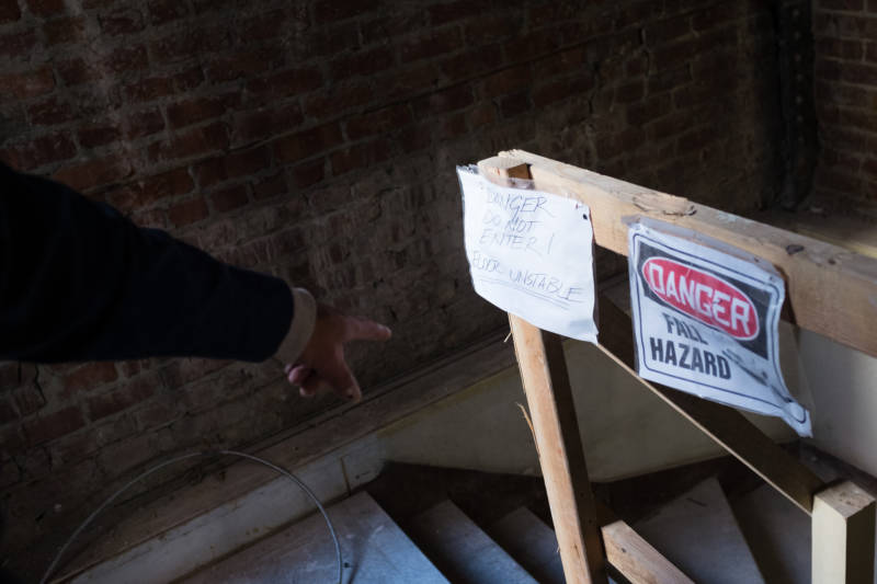Orlando Chavez points to a sign warning of an unstable floor in Hotel Travelers, the SRO where he has lived for nearly nine years, on Feb. 16, 2017. The building is being gutted and renovated and Chavez says he and the other few remaining low-income tenants are facing pressure to leave.