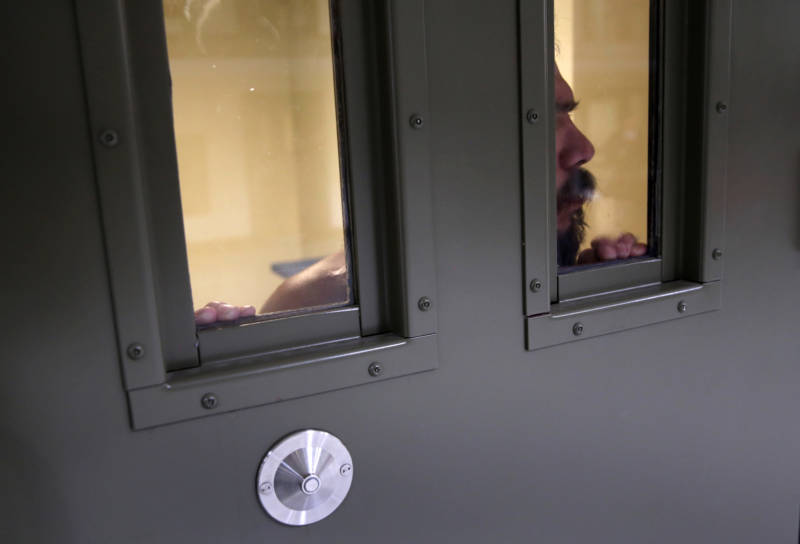 An immigrant detainee looks out from his 'segregation cell' at the Adelanto Detention Facility. The facility is owned by the for-profit GEO Group, which also pays contract fees to the city of Adelanto for every immigrant detained there.