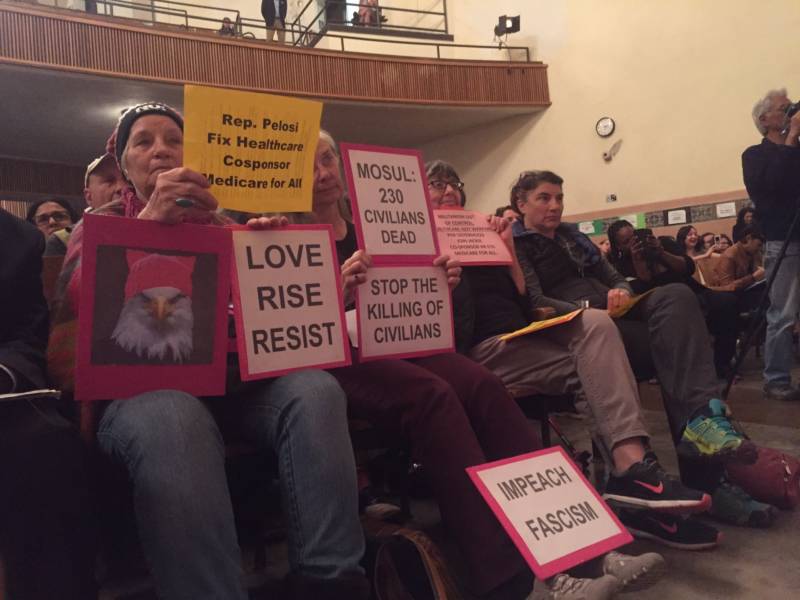 People hold signs at a town hall meeting held by House Minority Leader Nancy Pelosi (D-SF) and Rep. Jackie Speier (D-San Mateo) at Balboa High School in San Francisco on Saturday, March 25.