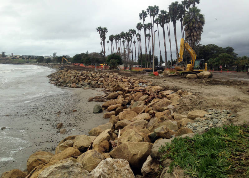 Workers install large boulders as rip rap to armor the shore against further erosion at Goleta Beach at negative tide.