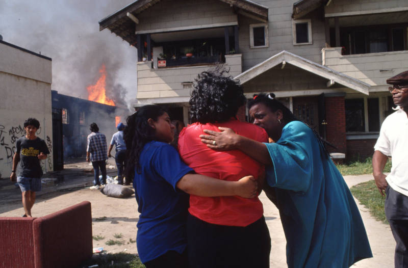 A woman is comforted on April 30, 1992, as she stands next to a home burning as a result of the riots.
