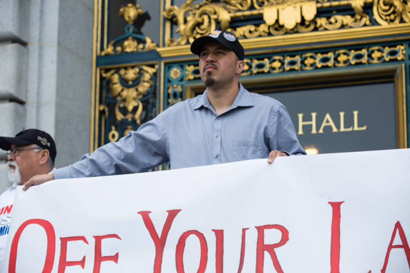 Sergio Estrella, a member of SEIU Local 87, held a banner during a press conference in front of San Francisco City Hall on April 24, 2017. He appeared with members of the May 1st Coalition, who were announcing their participation in the upcoming May Day protest.