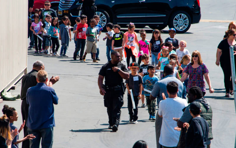 A police officer leads North Park elementary school students to be reunited with their parents following the shooting on Monday, April 10, 2017.
