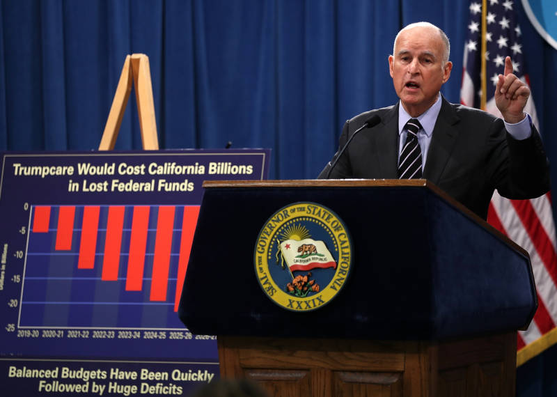 Gov. Brown stands next to a chart indicating the potential fiscal impacts of 'Trumpcare' on California on May 11, 2017.