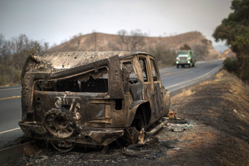 Firefighters pass a car that was destroyed by the Whittier Fire on July 9, 2017 near Santa Barbara