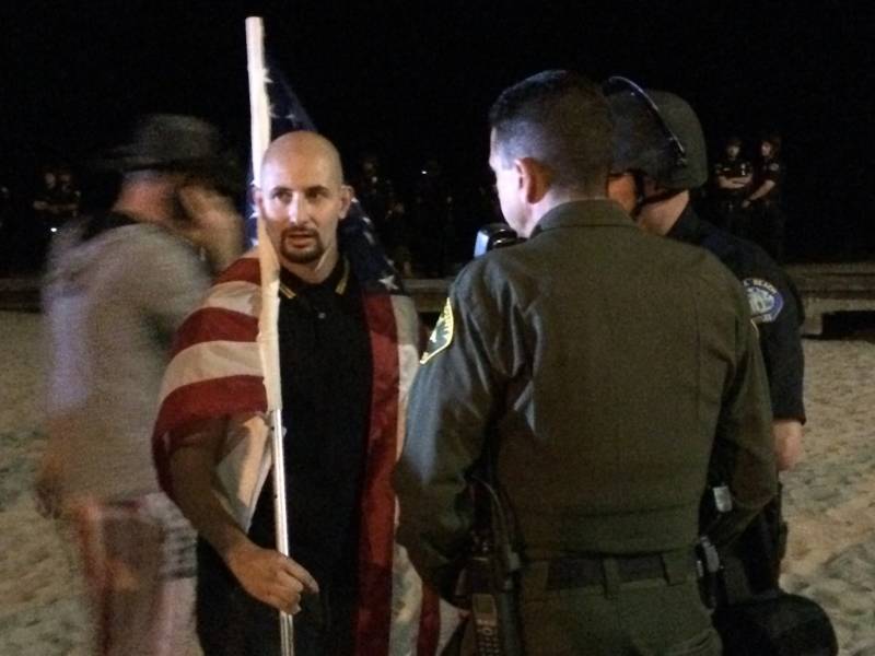 A man who uses the name Johnny Benitez for organizing, but whose legal name is Juan Cavidad, was a rally organizer. He holds an American flag just before he and others with the group America First! were escorted off the beach by police and sheriff’s deputies attempting to maintain a physical barrier between America First! demonstrators and the large group of counter-protesters who showed up at Laguna Beach Sunday.