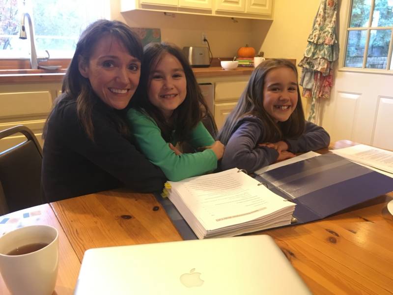 Carolynn Spezza sits at the kitchen table in her new home with her two daughters, a pile of insurance paperwork on the table in front of them.