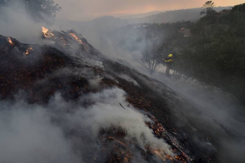 A firefighter puts out hotspots on a smoldering hillside in Montecito, California as strong winds blow smoke and embers inland on December 16, 2017 at the Thomas Fire.