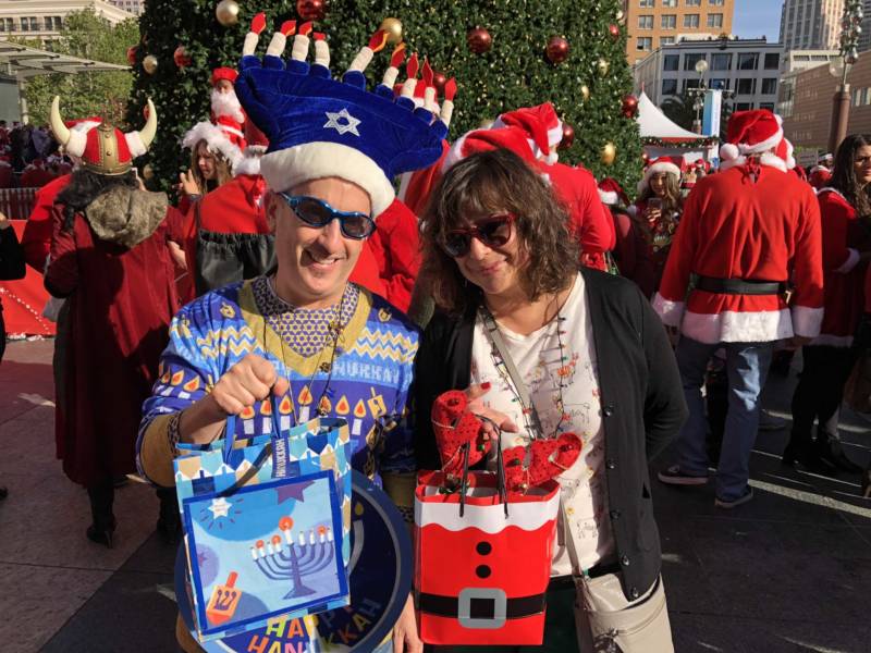 Andrew and Jennifer Fischer bring their mixed-religion marriage to SantaCon 2017 at San Francisco's Union Square. The Fischers say they've been going to the event on and off for years and love seeing the creativity of San Francisco on display. Andrew hands out dreidels and chocolate Hanukkah gelt while Jennifer hands out Christmas treats.