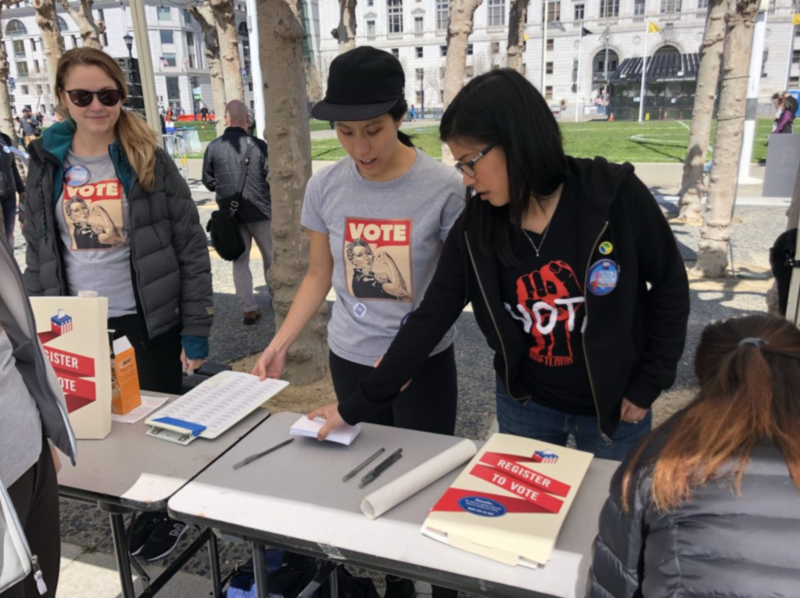 Volunteers Alison Goh and Jenny Tse register march participants to vote at the League of Women Voters booth in San Francisco's Civic Center Plaza.