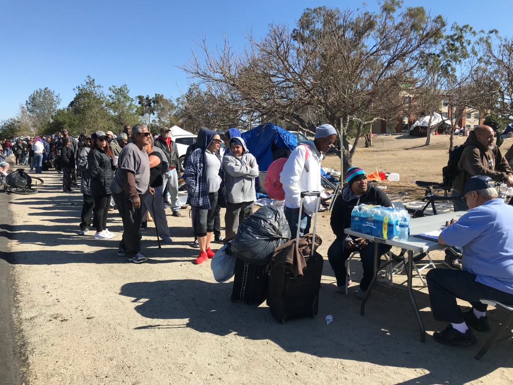 A line of homeless people at the Santa Ana riverbed wait to get connected with a motel room or shelter on Tuesday, Feb. 20, 2018.