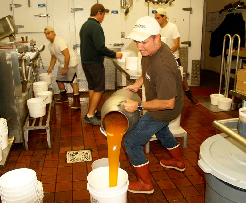 Chris Fosselman, forefront, pours salted caramel into a bucket to use in a mixer. John, center back, coordinates the hand packing with other staff members.