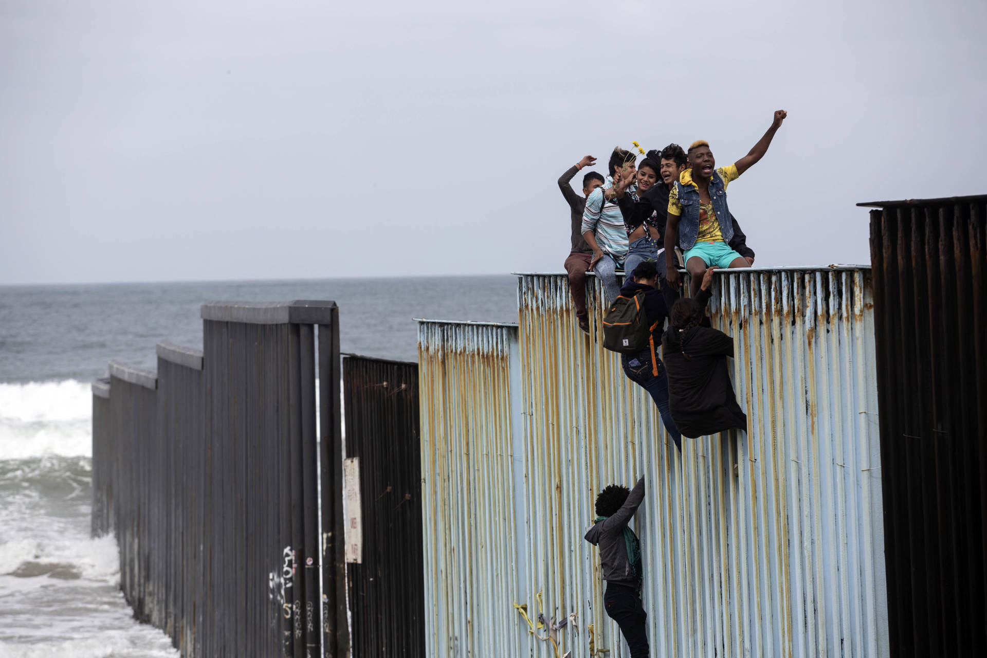 Some Central American migrants traveling in the "Migrant Via Crucis" caravan climbed the wall to sit and wave signs under the watchful eyes of U.S. Border Patrol agents at the US/Mexico Border at Tijuana's beaches, Baja California state, Mexico, on April 29, 2018.