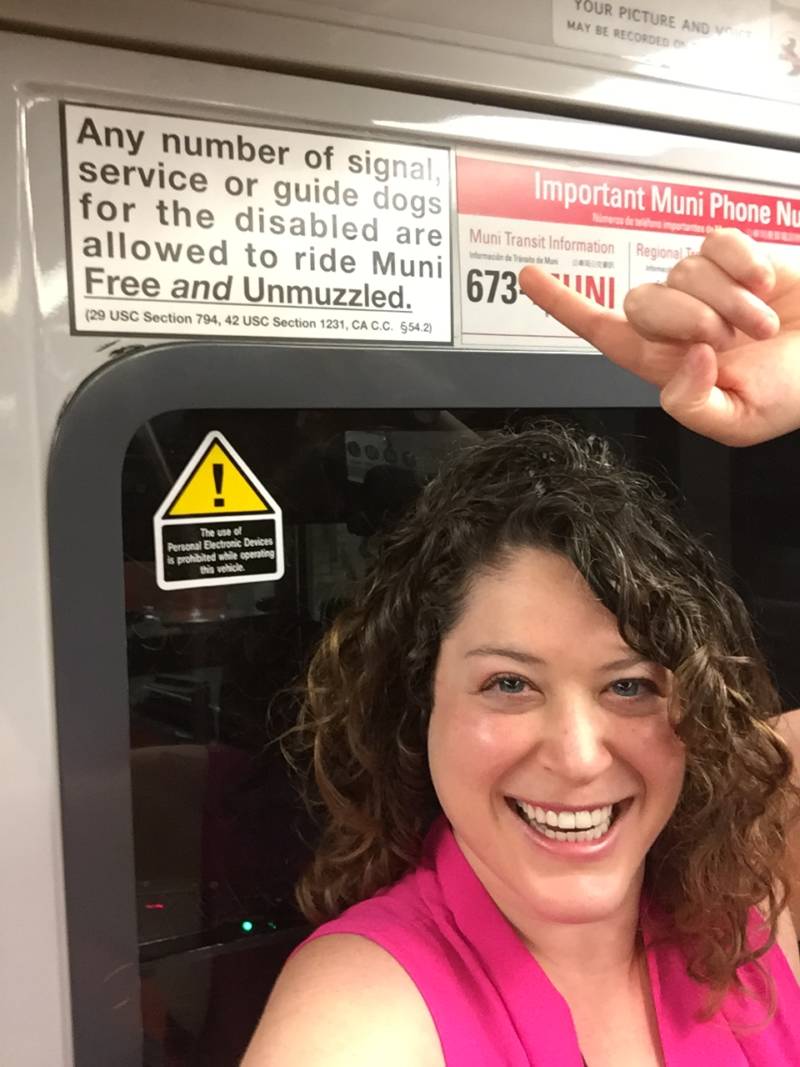 Bay Curious listener Rona Kramer stands next to a sign on the Muni Metro that says any number of service dogs can ride Muni.