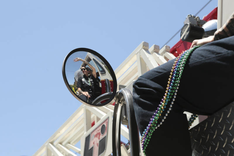 A firefighter waves to the crowd from the rear steering wheel of a firetruck.