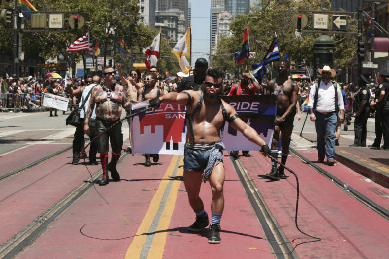 A member of the leather pride contingent makes his way down Market street while cracking two whips.