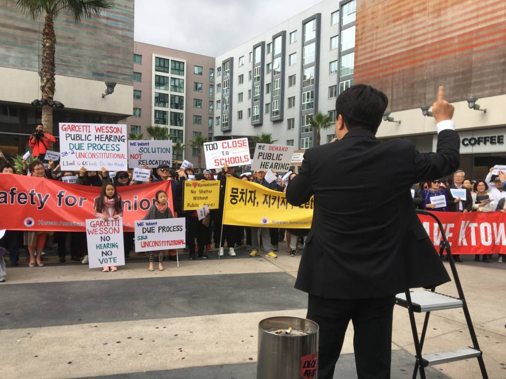 Jake Jeong, an attorney and community leader in Koreatown, leads the crowd in a call and response demanding a public hearing on the proposed temporary homeless shelter at 7th and Vermont.