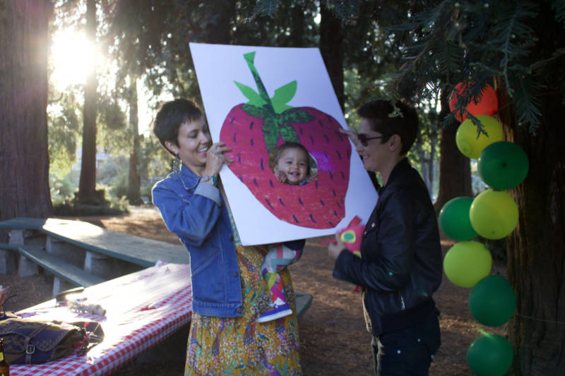 Oakland resident Noelle Kaplan (L) and her wife Stacey (R) with their daughter Sage at her first birthday party. The Kaplans moved to Oakland in part because they wanted to be somewhere with a lot of other queer families.