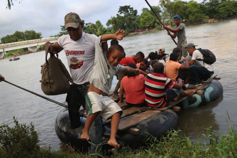 Migrant families cross into Mexico using a raft to avoid the Mexican officials perched on the bridge above the Suchiate River.