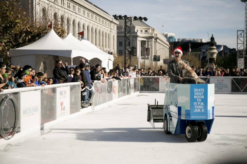 Figure skater and Olympic gold medalist Brian Boitano rides around the rink on a Zamboni with his dog Hunter before charging through the ribbon to officially open the rink. 
