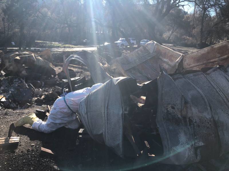 An EPA worker crawls into the remnants of a mobile home burned by the Camp Fire to look for hazardous material to remove. 