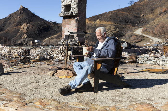Holding a cigar, Gary Jones sits where his house once stood, in a wooden porch chair that somehow wasn't destroyed. Jones lost three of his five dogs in the flames and came back the next day to bury them. His horse was found alive up the hill and is recovering from burns.
