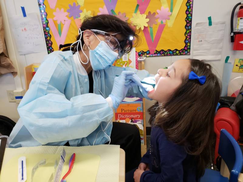 Dental hygienist Deborah Delfino cleans the teeth of a preschooler in Lathrop, CA.
