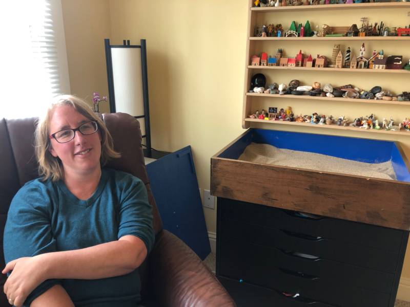 Psychotherapist Orit Weksler poses in her Berkeley office with her sand tray and shelves of figurines.