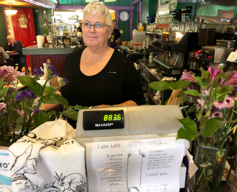 Mary Pulskamp wears a safety pin on her shirt while working the register at Rosebud's Cafe. The signs below signify that the cafe is a safe space for those who feel persecuted.