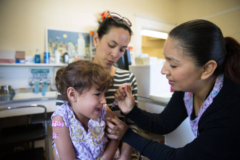 Alexis Tjian holds her 5-year-old daughter as she receives a vaccination from Etzel Rubio at Berkeley Pediatrics. Senate Bill 276 would bar physicians from charging for vaccine exemptions, and allow the state to review certain exemptions that have been granted.