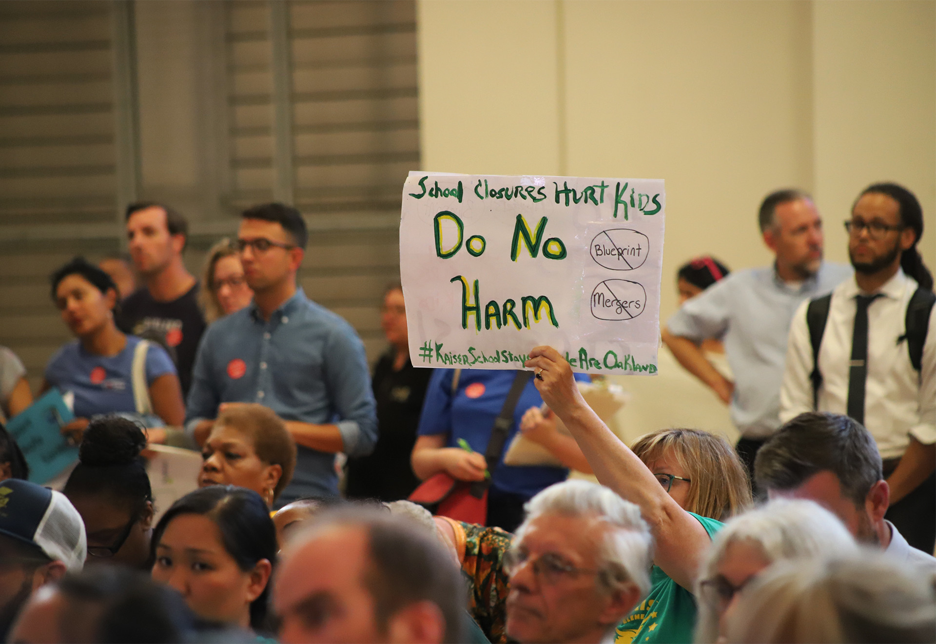 An attendee at an Aug. 28, 2019 OUSD board meeting holds a sign reading "Do Not Harm" in opposition to the district's plan to merge Henry J. Kaiser Jr. Elementary with another school.
