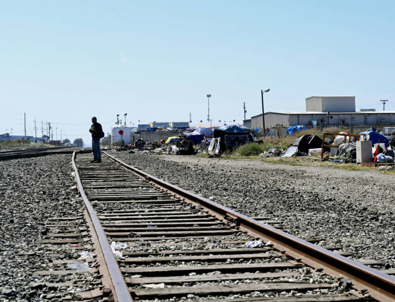 A man walks the railroad tracks along the edge of a homeless encampment where he stays on June 12, 2019.
