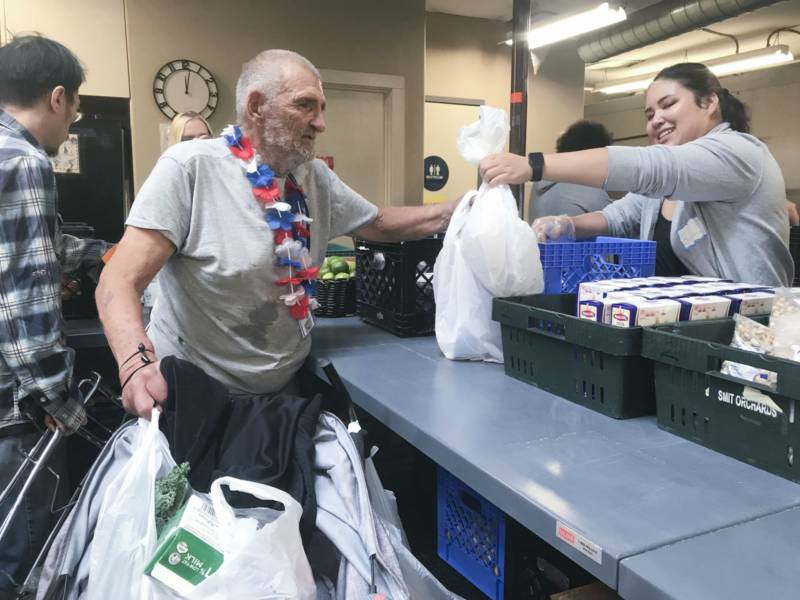 Photo of Richard Valentin standing in line to pick up food from the River City Food Bank. He places the bags of food on his walker.