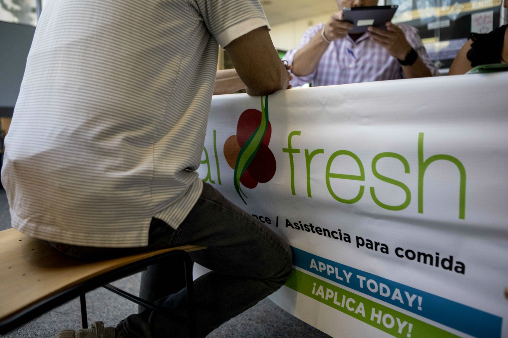 Photo of a man signing a document at a table with an ad that says CalFresh.
