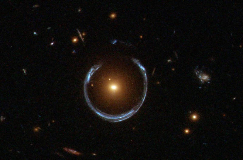 A visible-light image of a gravitational lens captured by the Hubble Space Telescope. The central galaxy, LRG 3-757, is serving as a gravitational lens producing a distorted "ring" image of a more distant blue galaxy, positioned behind. 