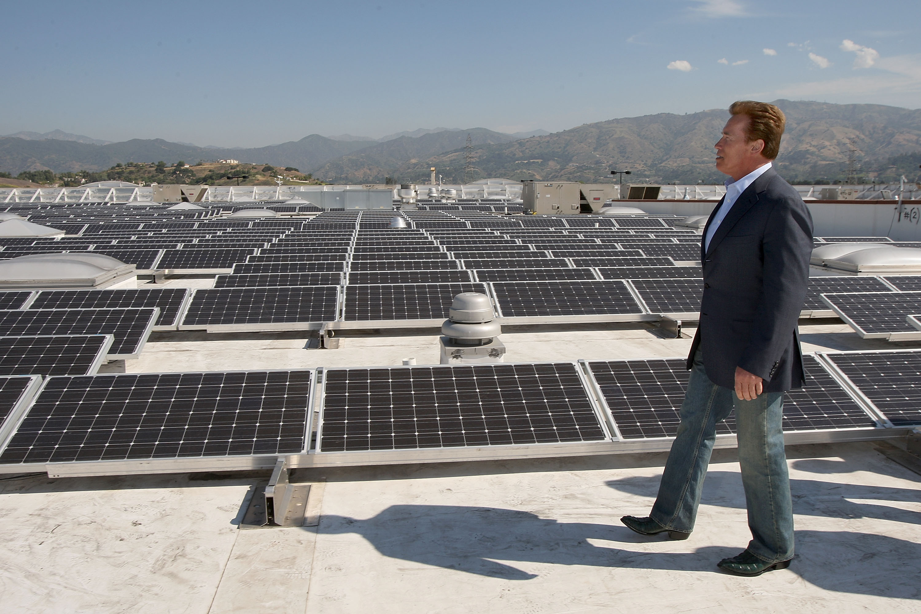 Gov. Schwarzenegger walks on top of a roof surrounded by solar panels.