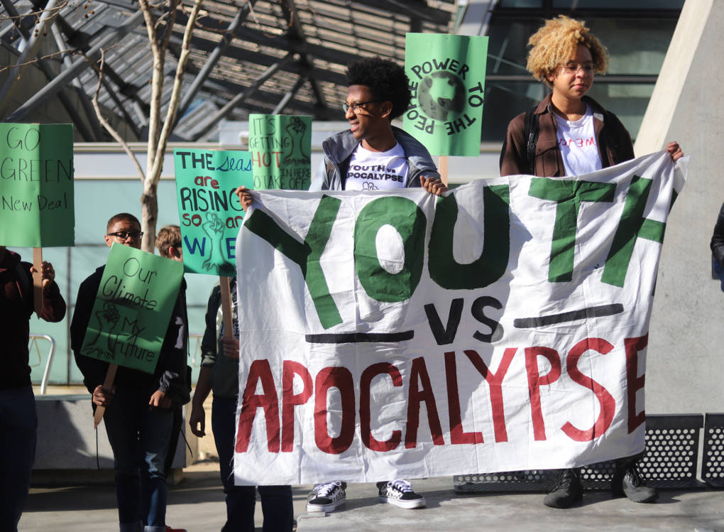 Students Bruck and Jai hold up a banner that says "Youth vs Apocalypse" outside of the office building of Nancy Pelosi in downtown San Francisco on Friday March 15, 2019. (Lindsey Moore/KQED)